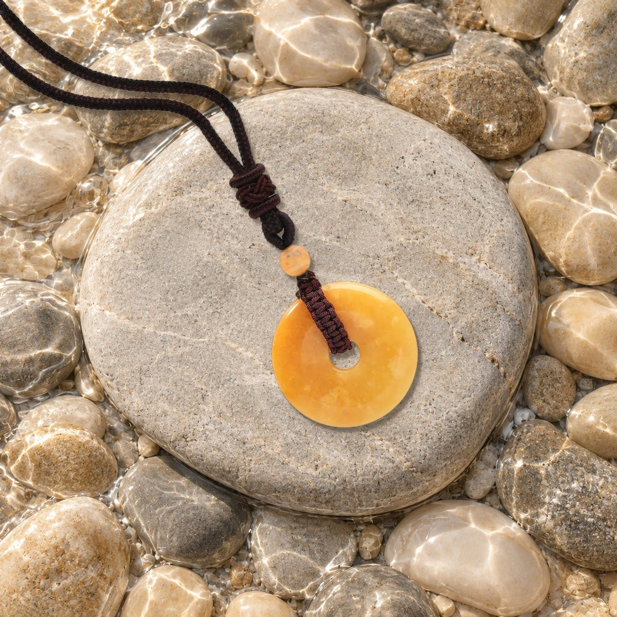 Collier donut jade jaune Nuée posé sur un galet de rivière