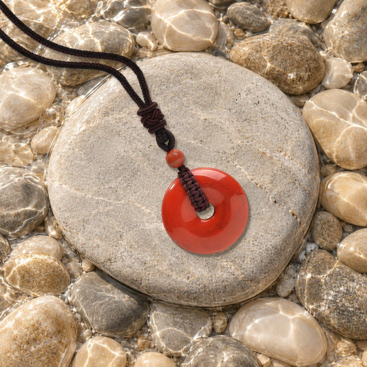 Collier donut jaspe rouge Nuée posé sur un galet de rivière