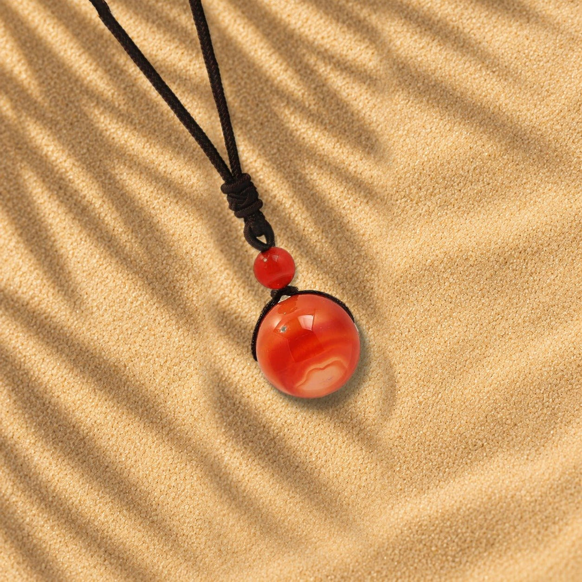 Collier cornaline Orbe, pendentif sphère en pierre naturelle posé sur le sable