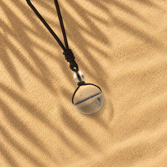 Collier cristal de roche Orbe, pendentif sphère en pierre naturelle posé sur le sable