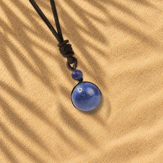 Collier lapis-lazuli Orbe, pendentif sphère en pierre naturelle posé sur le sable