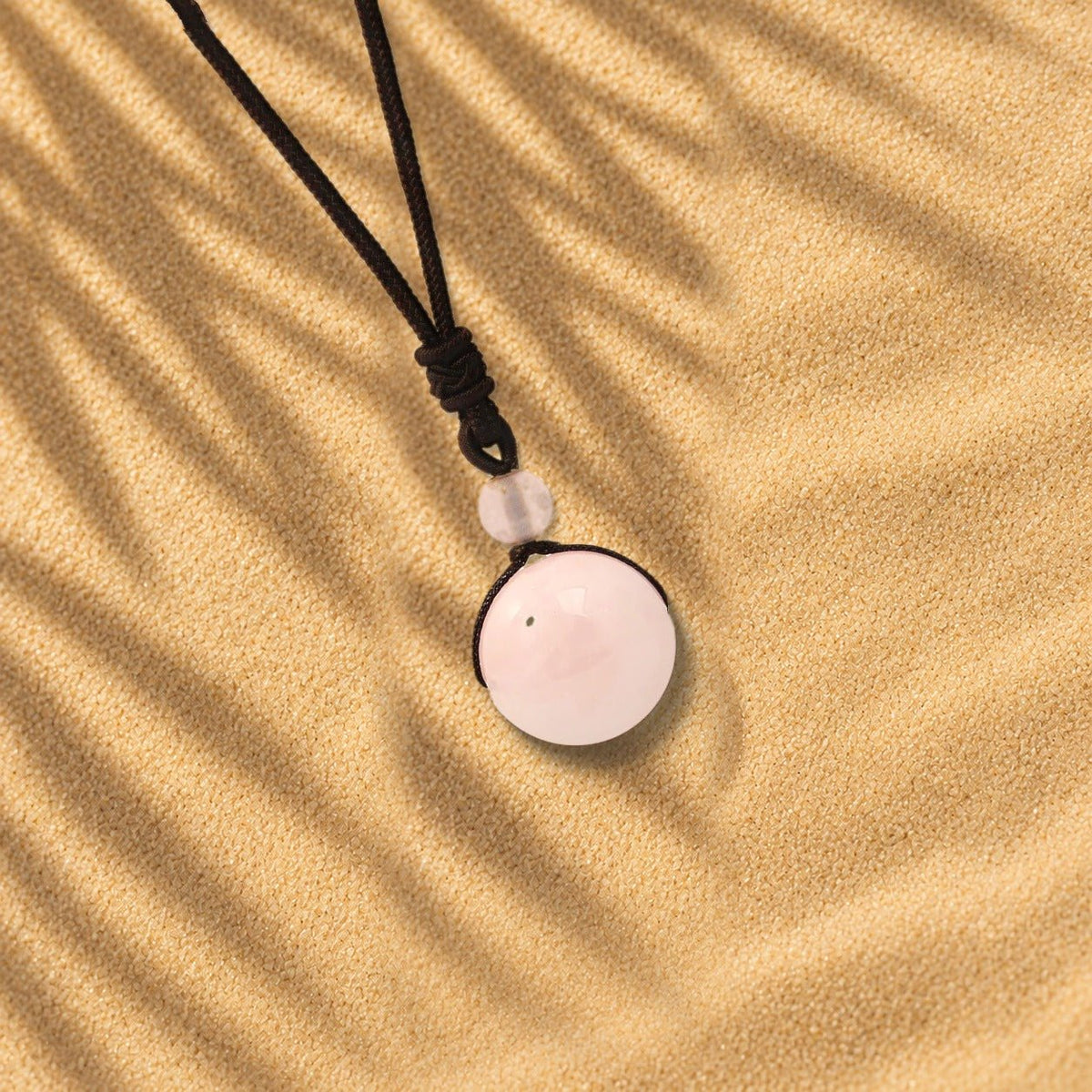 Collier quartz rose Orbe, pendentif sphère en pierre naturelle posé sur le sable